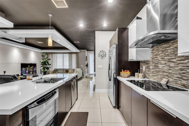 kitchen featuring wall chimney range hood, sink, appliances with stainless steel finishes, dark brown cabinets, and decorative light fixtures