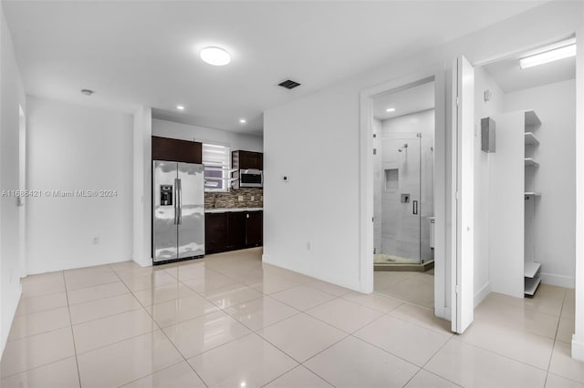 interior space featuring dark brown cabinetry, stainless steel appliances, backsplash, and light tile patterned floors