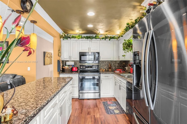 kitchen with appliances with stainless steel finishes, white cabinetry, dark stone countertops, and decorative light fixtures