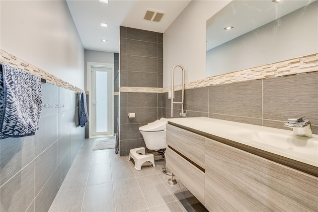 bathroom with toilet, vanity, tile patterned floors, and tile walls