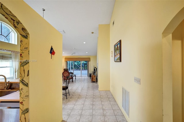 hall with a towering ceiling, a wealth of natural light, and light tile patterned flooring