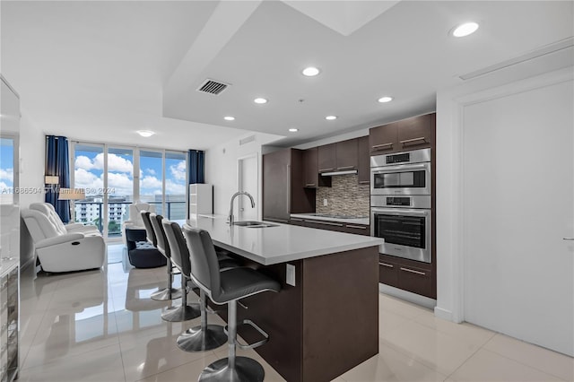 kitchen with a breakfast bar, sink, decorative backsplash, light tile patterned floors, and an island with sink