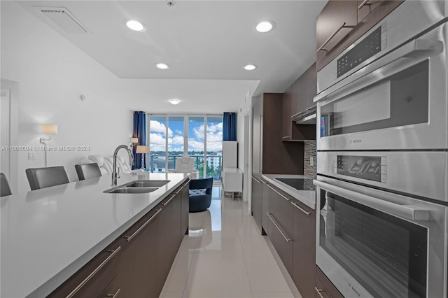 kitchen with dark brown cabinetry, sink, a kitchen breakfast bar, black electric stovetop, and light tile patterned flooring