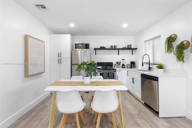 kitchen with light hardwood / wood-style flooring, appliances with stainless steel finishes, sink, white cabinets, and a breakfast bar