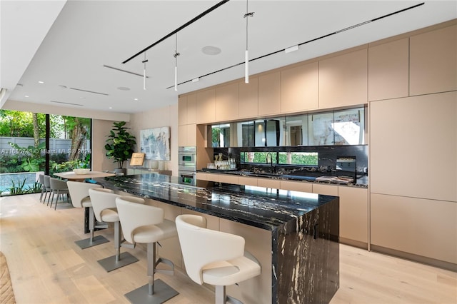 kitchen featuring dark stone counters, a spacious island, decorative light fixtures, light hardwood / wood-style floors, and stainless steel double oven