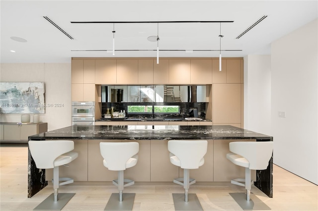 kitchen featuring hanging light fixtures, a breakfast bar area, dark stone counters, and light hardwood / wood-style flooring