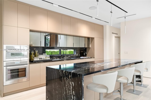 kitchen featuring decorative backsplash, dark stone counters, sink, decorative light fixtures, and a center island