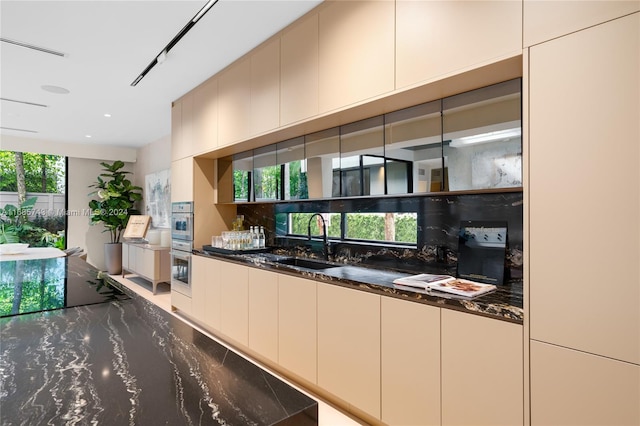 kitchen with decorative backsplash, double oven, dark stone countertops, and sink