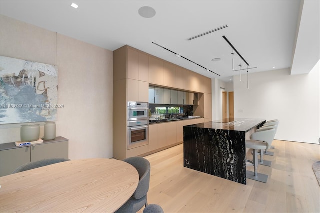 kitchen featuring backsplash, track lighting, black electric stovetop, light wood-type flooring, and stainless steel double oven