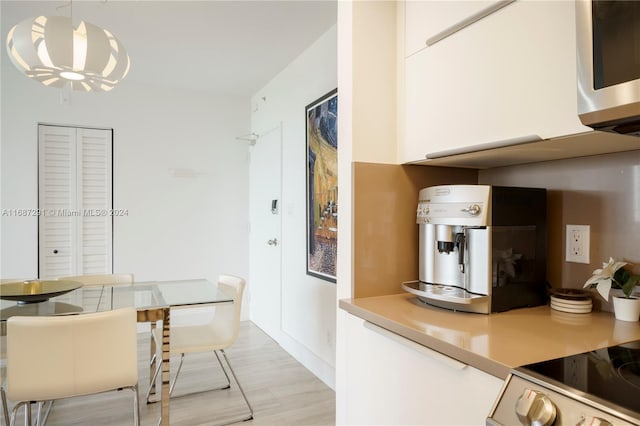 kitchen with a notable chandelier, white cabinetry, light wood-type flooring, and pendant lighting