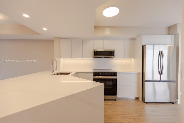 kitchen featuring white cabinetry, stainless steel appliances, a sink, and light countertops