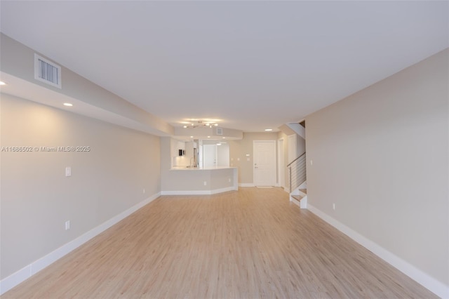 unfurnished living room with light wood-style flooring, visible vents, stairway, and baseboards