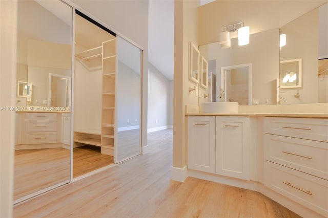 bathroom with a spacious closet, baseboards, wood finished floors, and vanity