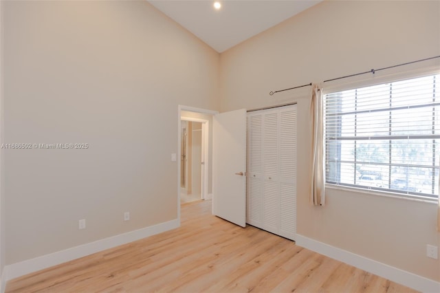 unfurnished bedroom featuring light wood-style floors, a closet, vaulted ceiling, and baseboards