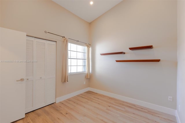 unfurnished bedroom with light wood finished floors, baseboards, vaulted ceiling, and a closet