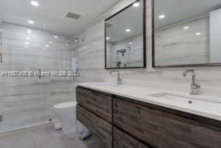 bathroom featuring toilet, vanity, a tile shower, and tile walls