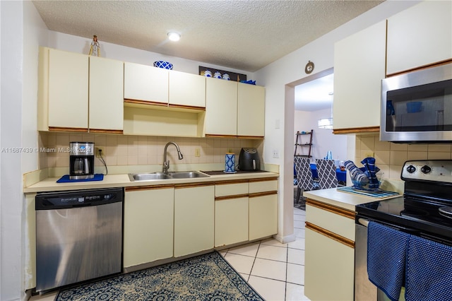 kitchen with sink, appliances with stainless steel finishes, a textured ceiling, light tile patterned floors, and backsplash