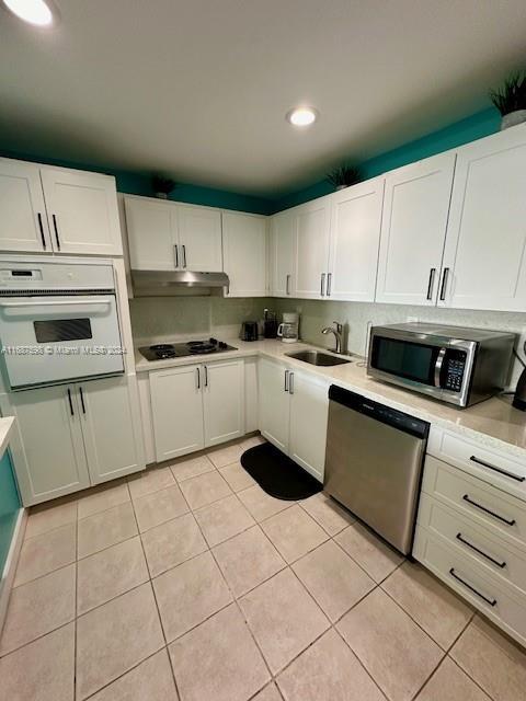 19370 Collins Ave Unit 1203, Sunny Isles Beach, FL 33160 - kitchen with stainless steel appliances, light tile patterned flooring, light countertops, under cabinet range hood, and white cabinets