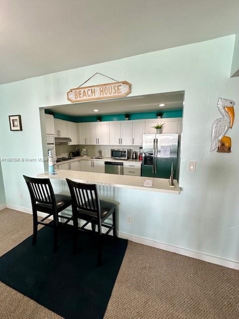 19370 Collins Ave Unit 1203, Sunny Isles Beach, FL 33160 - kitchen with stainless steel appliances, white cabinetry, dark carpet, light countertops, and a peninsula