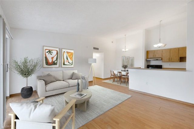 living room featuring light wood-type flooring, high vaulted ceiling, and an inviting chandelier