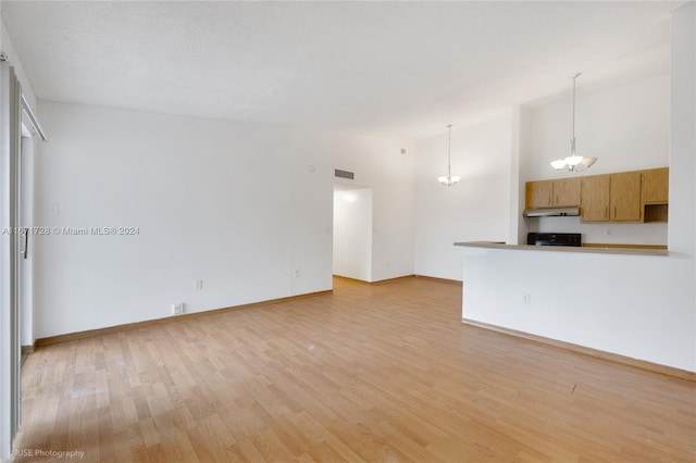 unfurnished living room with a textured ceiling, light hardwood / wood-style flooring, a chandelier, and a high ceiling