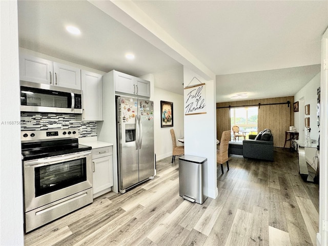 kitchen with backsplash, appliances with stainless steel finishes, light hardwood / wood-style flooring, and white cabinets