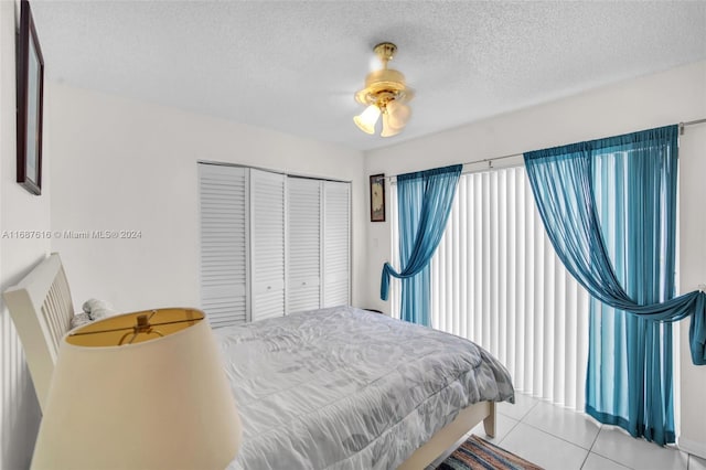 bedroom with a textured ceiling, light tile patterned floors, ceiling fan, and a closet