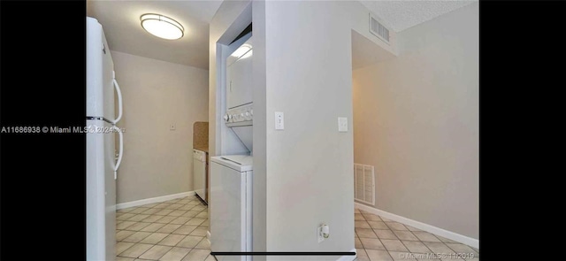 kitchen with stacked washing maching and dryer, white fridge, and light tile patterned floors