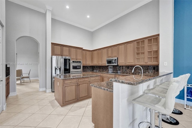 kitchen featuring a towering ceiling, ornamental molding, dark stone counters, and appliances with stainless steel finishes