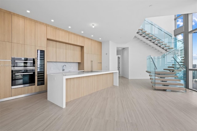 kitchen featuring stainless steel double oven, sink, a center island, light wood-type flooring, and light brown cabinetry