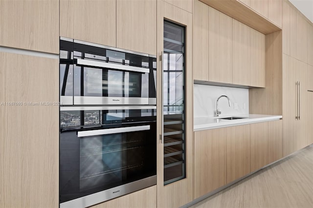 kitchen with sink, light brown cabinetry, backsplash, and stainless steel double oven