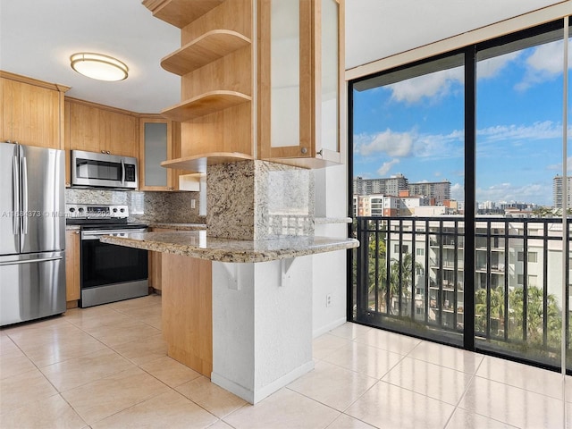 kitchen with tasteful backsplash, light tile patterned floors, appliances with stainless steel finishes, light stone countertops, and a kitchen bar