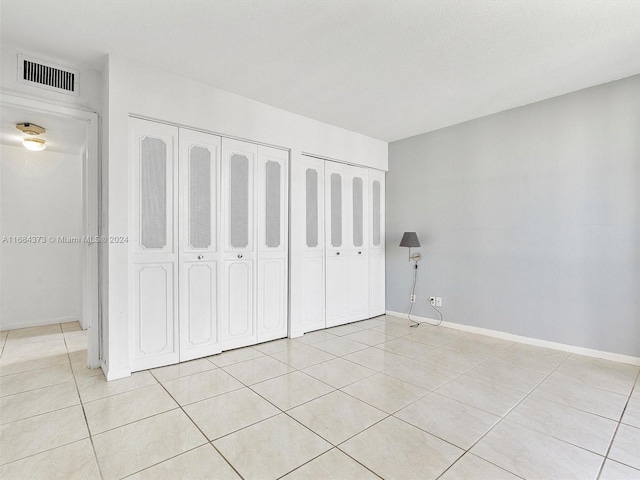 unfurnished bedroom with light tile patterned flooring and two closets