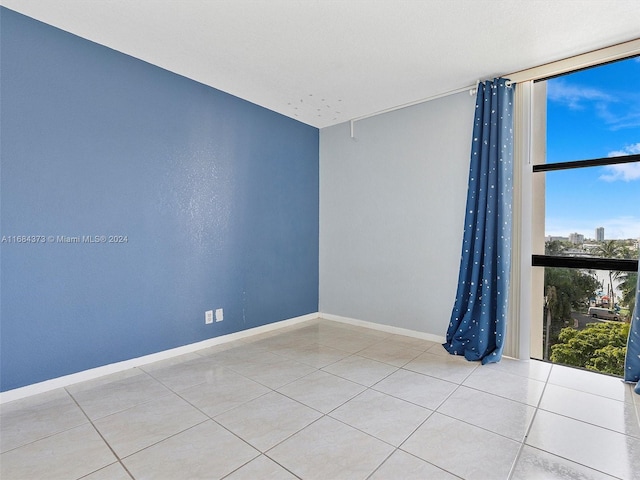 tiled empty room featuring a wall of windows