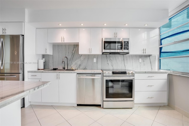 kitchen with sink, decorative backsplash, light stone countertops, appliances with stainless steel finishes, and white cabinetry