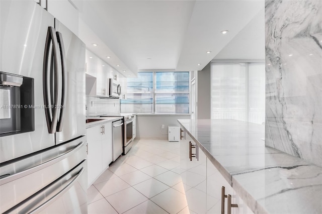 kitchen featuring white cabinets, light tile patterned floors, light stone countertops, and appliances with stainless steel finishes