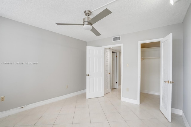 unfurnished bedroom with a textured ceiling, ceiling fan, a spacious closet, a closet, and light tile patterned flooring