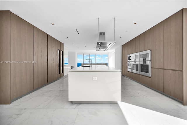 kitchen featuring a kitchen island with sink, wood walls, sink, and stainless steel double oven