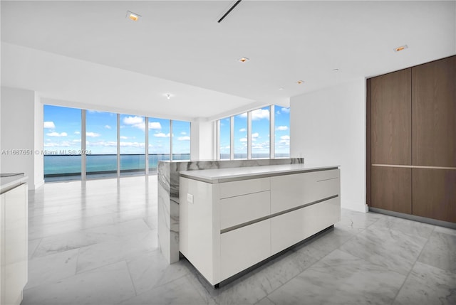 interior space featuring white cabinets, a water view, a kitchen island, and floor to ceiling windows