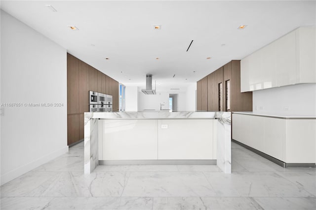 kitchen featuring light stone counters, white cabinetry, exhaust hood, wooden walls, and a spacious island