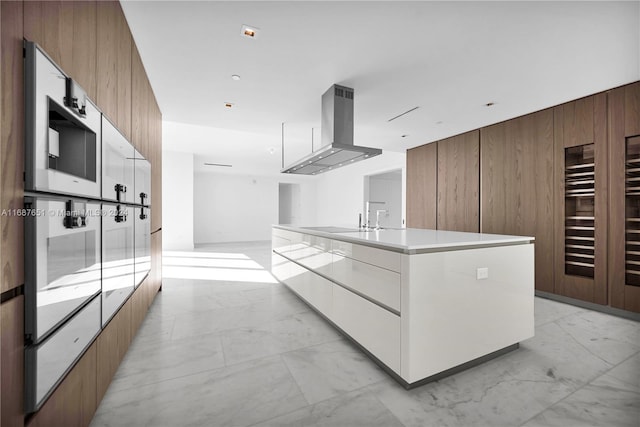 kitchen with wooden walls, a kitchen island with sink, exhaust hood, and white cabinets