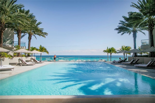 view of pool with a patio, a water view, and a view of the beach