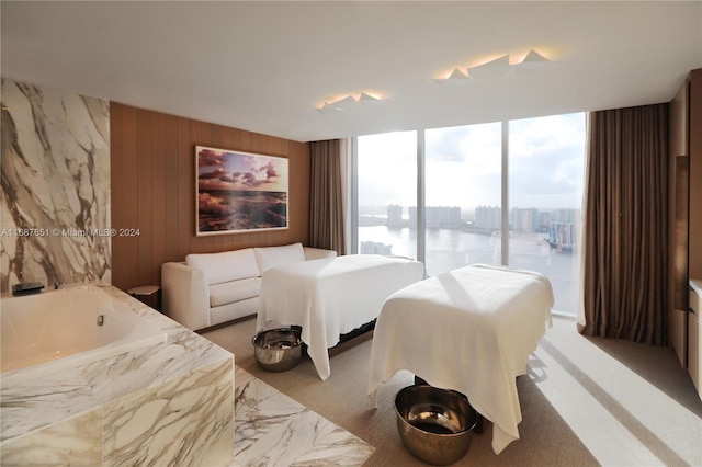 carpeted bedroom with access to exterior, a water view, wooden walls, and floor to ceiling windows