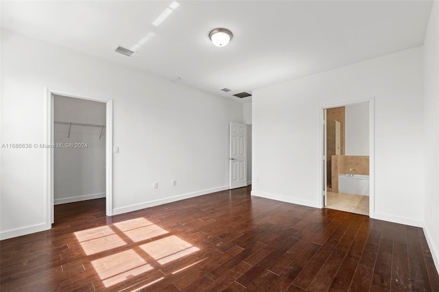 unfurnished bedroom featuring a closet, a walk in closet, ensuite bathroom, and dark hardwood / wood-style flooring