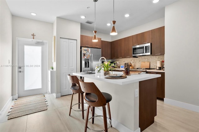 kitchen with appliances with stainless steel finishes, backsplash, a kitchen breakfast bar, pendant lighting, and a center island with sink