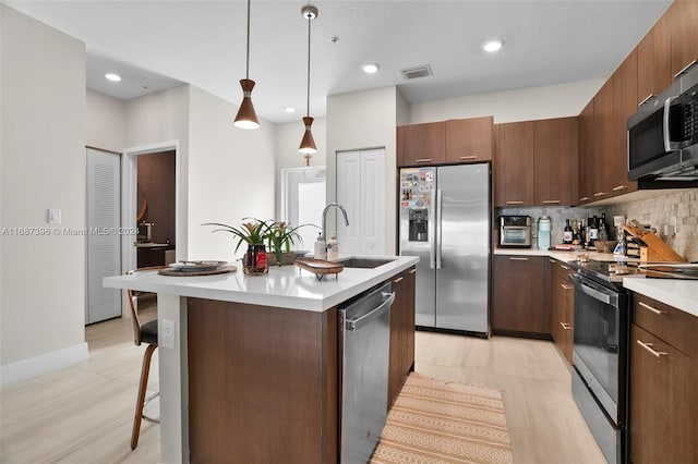 kitchen featuring decorative backsplash, an island with sink, stainless steel appliances, sink, and pendant lighting