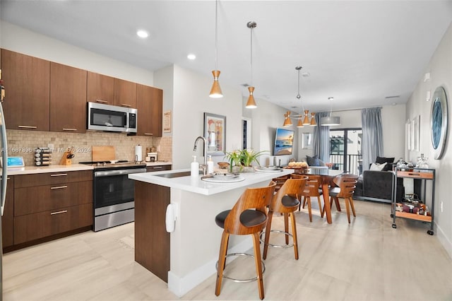 kitchen with a kitchen island with sink, stainless steel appliances, sink, a kitchen bar, and decorative light fixtures