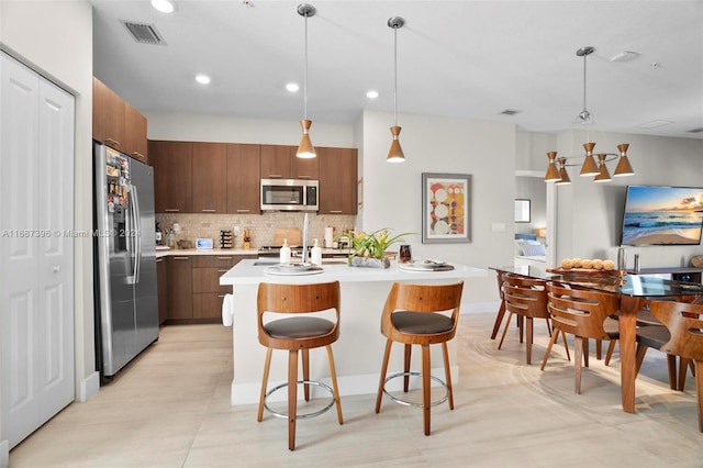 kitchen with tasteful backsplash, a center island with sink, a kitchen bar, stainless steel appliances, and decorative light fixtures