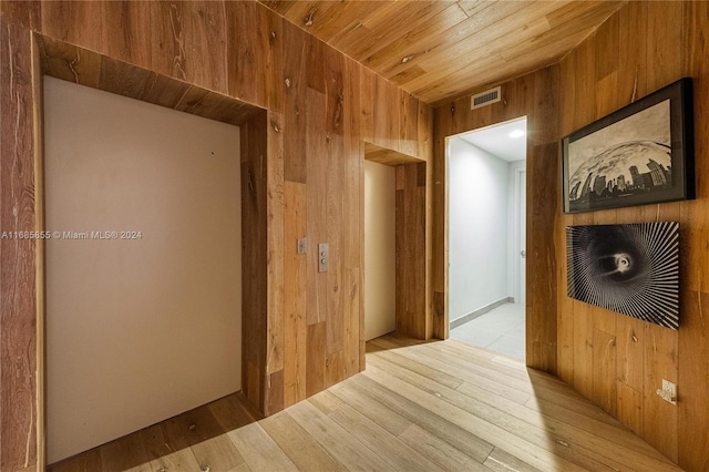 corridor with wood walls, light hardwood / wood-style flooring, and wood ceiling