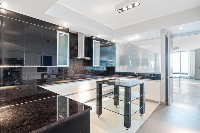 kitchen with white cabinetry, wall chimney range hood, dark stone countertops, decorative backsplash, and light tile patterned flooring